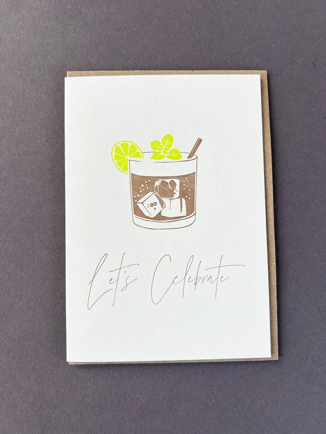 A metallic bronze Mojito Drink with lime coloured garnish and "Let's  Celebrate"  beautifully written in a modern calligraphy.