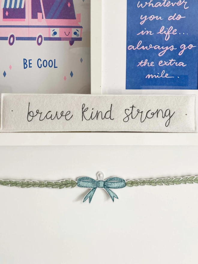 Brave Kind Strong Felt Embroidered Sign on a shelf with bow decoration