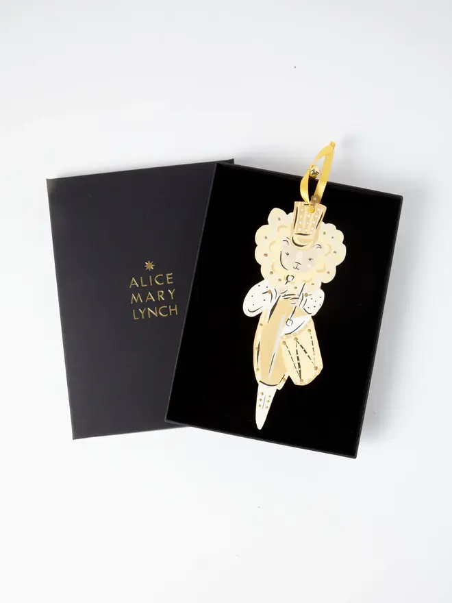 Lion Drummer Tree Dancer. wooden hanging lion drummer decoration in an open black gift box embossed "alice mary lynch" in gold, with gold top hat, cream mane, gold tunic and drum, yellow ribbon with a jingle bell