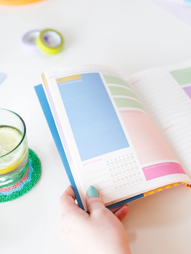 A close up of inside daily planner shows space for habit tracking, weekly goals, and a colourful place to plan a reward for the week