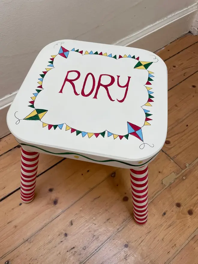 personalised hand-painted nursery stool. a small white stool with red and white striped legs, painted with 'rory' on top.