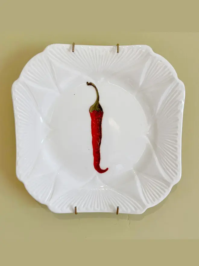 Oil Painted Chilli On Antique Tea Plate, hanging on a yellow wall. 