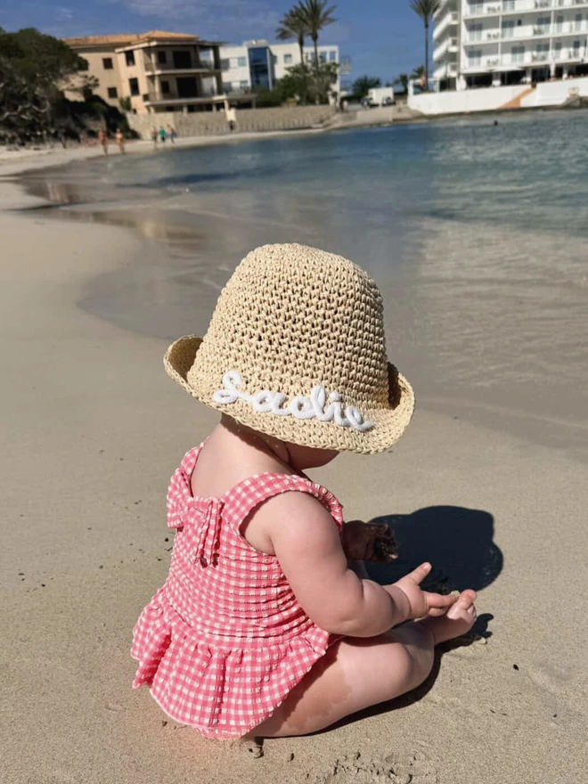 Baby Toddler personalised straw hat, worn by baby sitting on beach