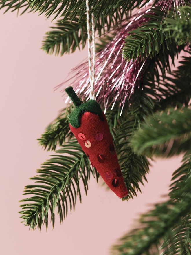 A red velvet and sequinned chilli pepper ornament on a tree