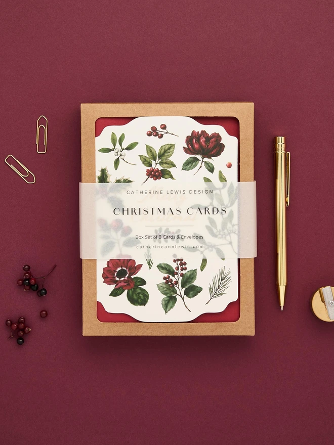 Box of 8 cards, with red envelopes. gold foil and die-cut shape cards with greens and red botanicals