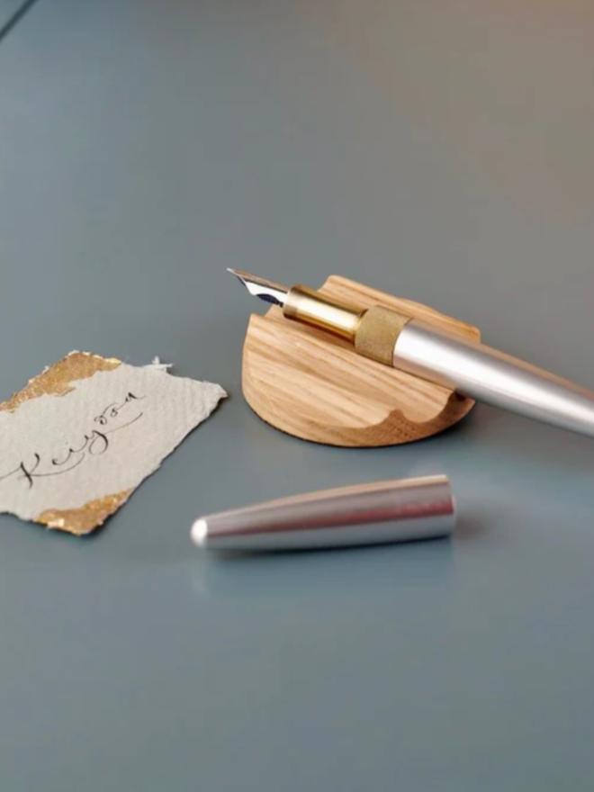 Tani Wooden Pen Rest. The rest, in Oak, is shown used with a pen sat on top.