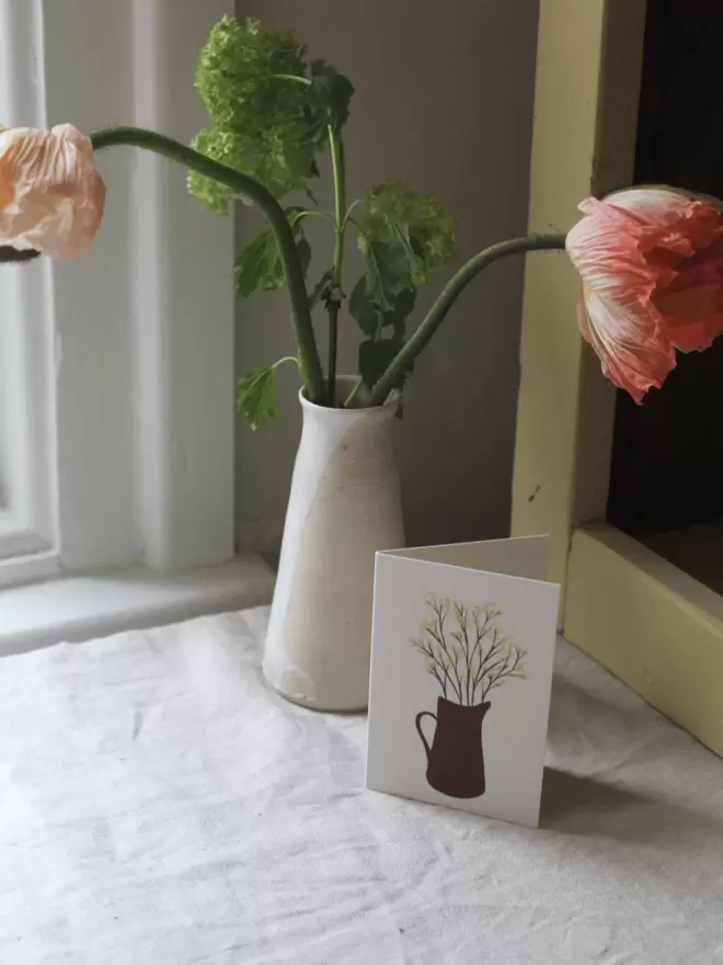 card with yellow mimosas in a vase, next to a vase of fresh Icelandic poppies. 