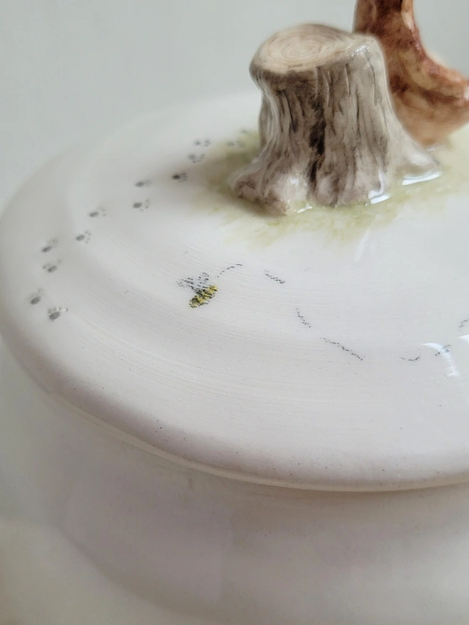 close up of a hand painted bee on the top of a ceramic honey pot with tiny bear paw prints