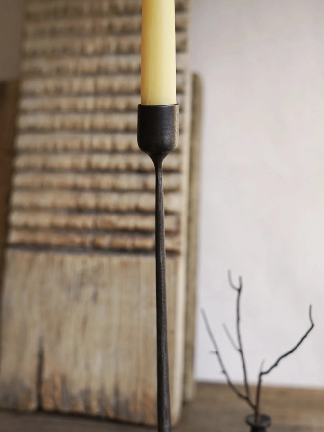 Forged Steel Candle Stick, a metal candle stick sitting on a wooden surface against a wood backdrop. 