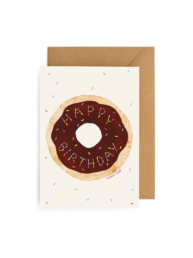 Scratch and sniff happy birthday greeting card featuring a chocolate scented doughnut with rainbow sprinkles spelling out Happy Birthday! Comes with 100% recycled kraft envelope.