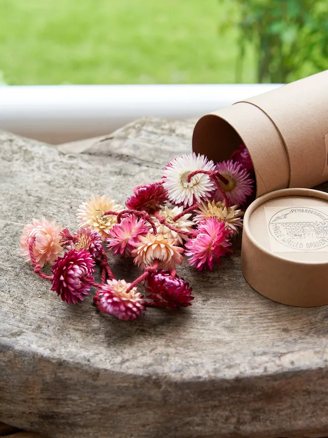 Pretty pink dried flower garland packaged in a brown tube box placed on a wooded table outside on the grass 