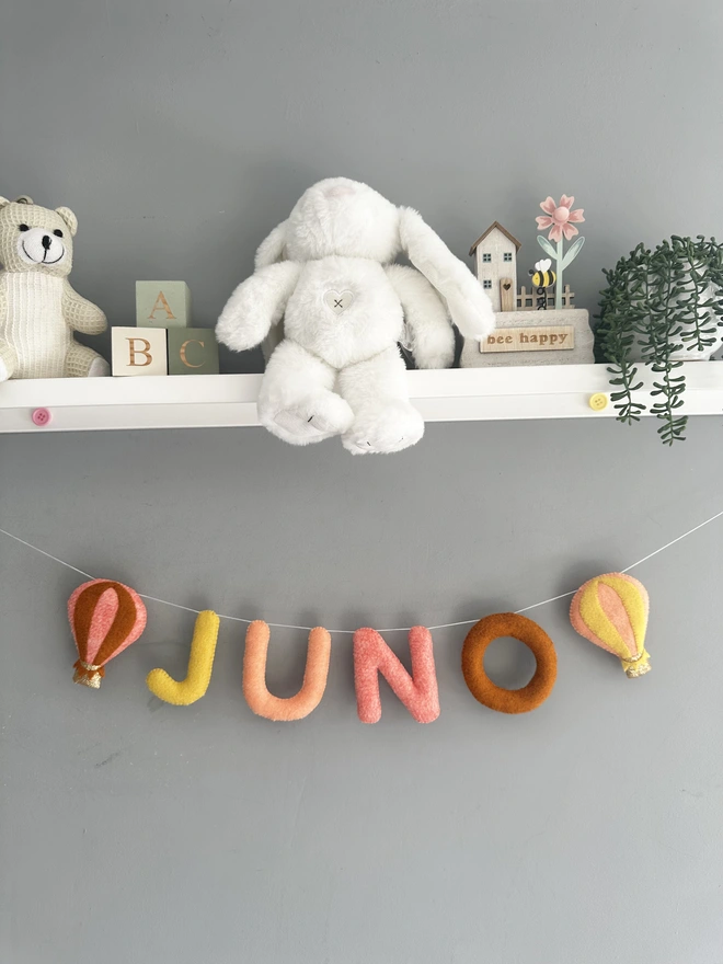 Personalised Name Icon Garland, a child’s name banner hanging from a white shelf, nursery decoration, baby, gift