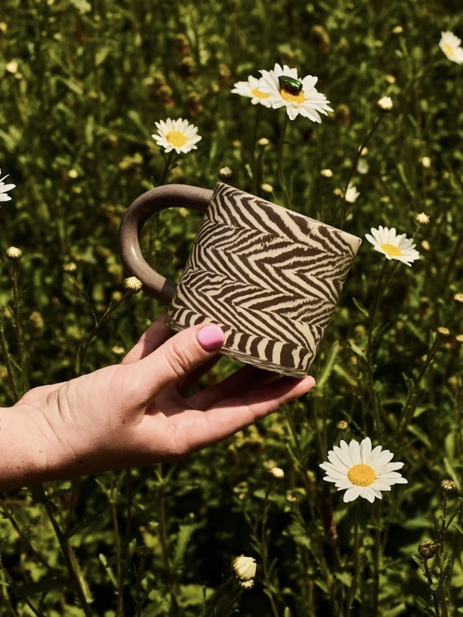 Herringbone Chunky Mug, a colourful mug held above a grassy backdrop. 
