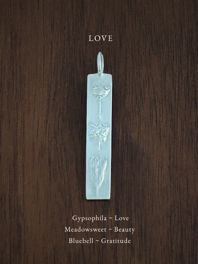 Love bar pendant in sterling silver on a dark background with the meaning of the flowers written in white