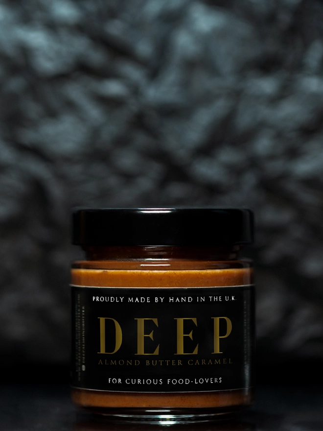 Jar of almond butter caramel against textured black background