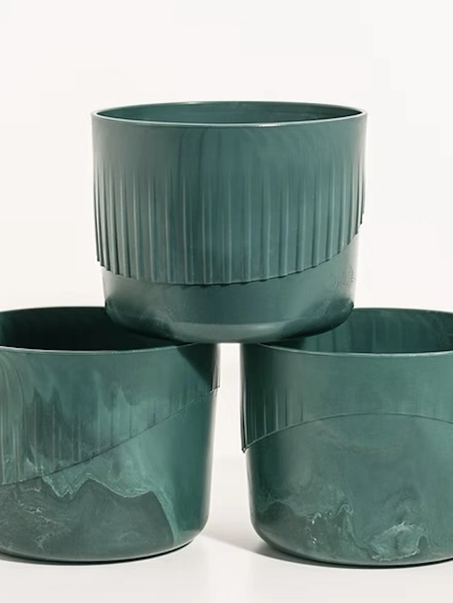 Ocean Plastic Plant Pot Small, a group of green recycled plant pots sitting on a white surface against a plain backdrop. 