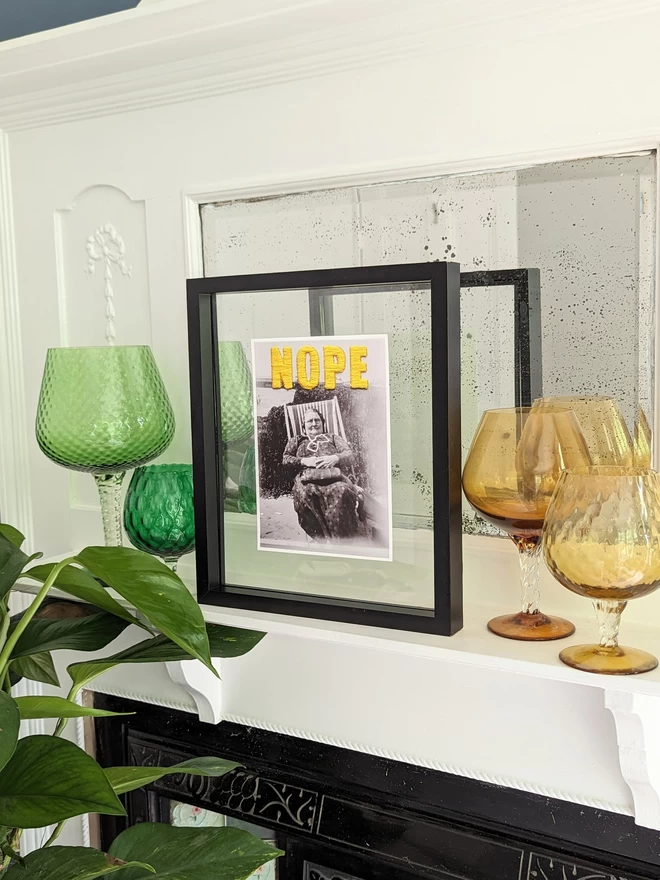  B & W photo print of woman with yellow embroidered ‘nope’ framed on mantlepiece
