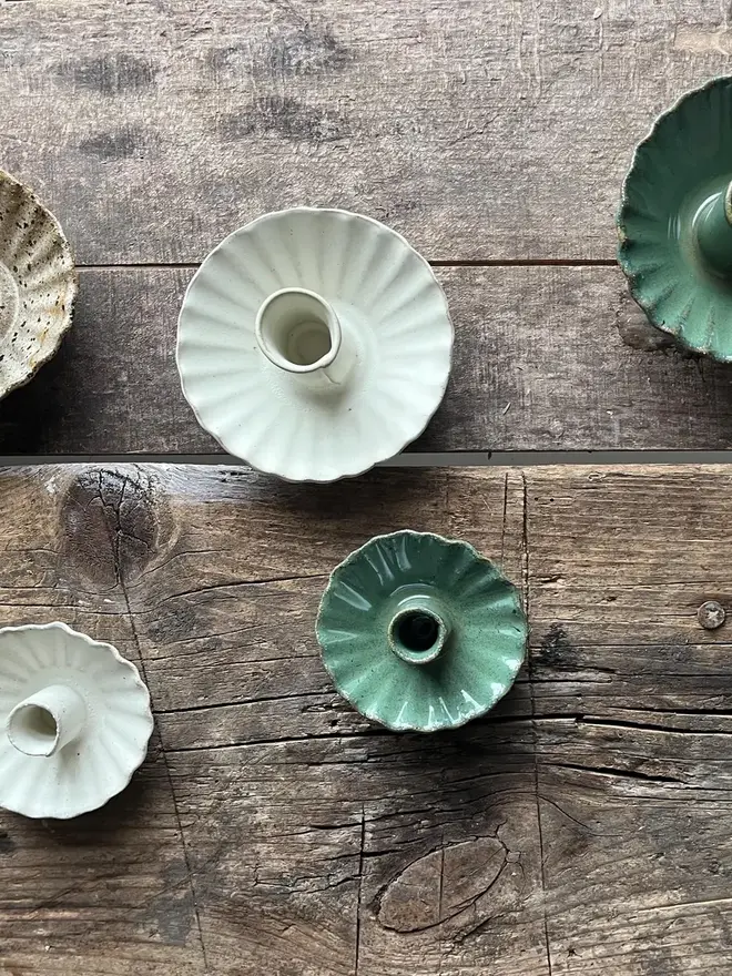 Handmade Green Ceramic Candlestick Holder, a pair of green candlestick holders sitting on a wooden surface. They are accompanied by other ceramic candlestick holders. 