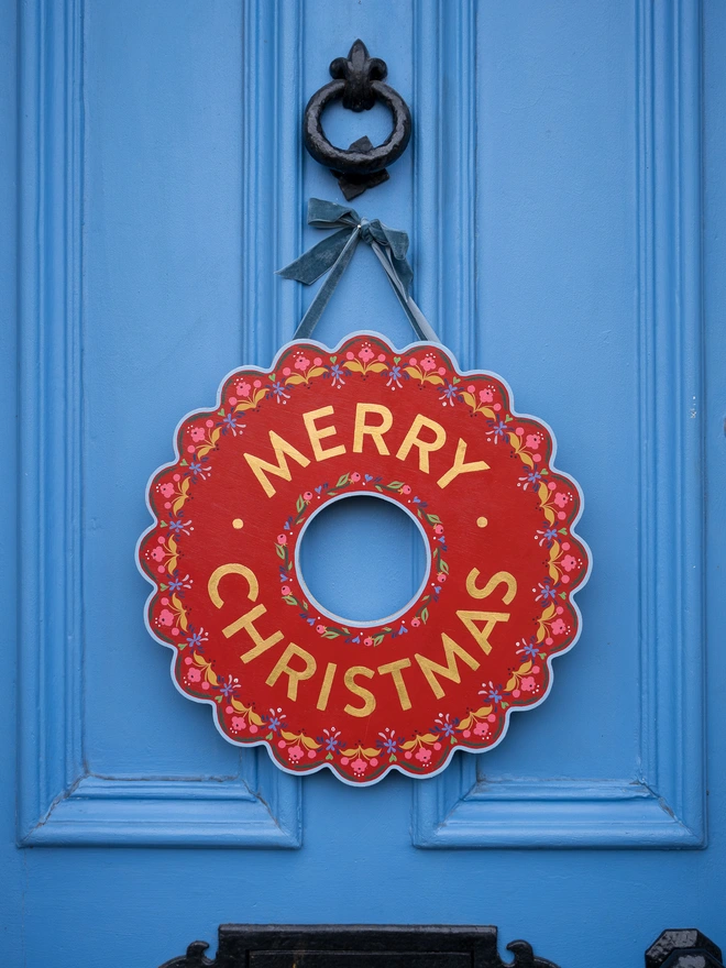 Red Hand painted Christmas Wreath with red lettering and gold leaf lettering on a blue front door