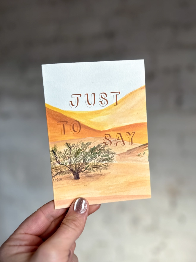 a greetings card featuring an illustration of a desert landscape with the text “just to say”