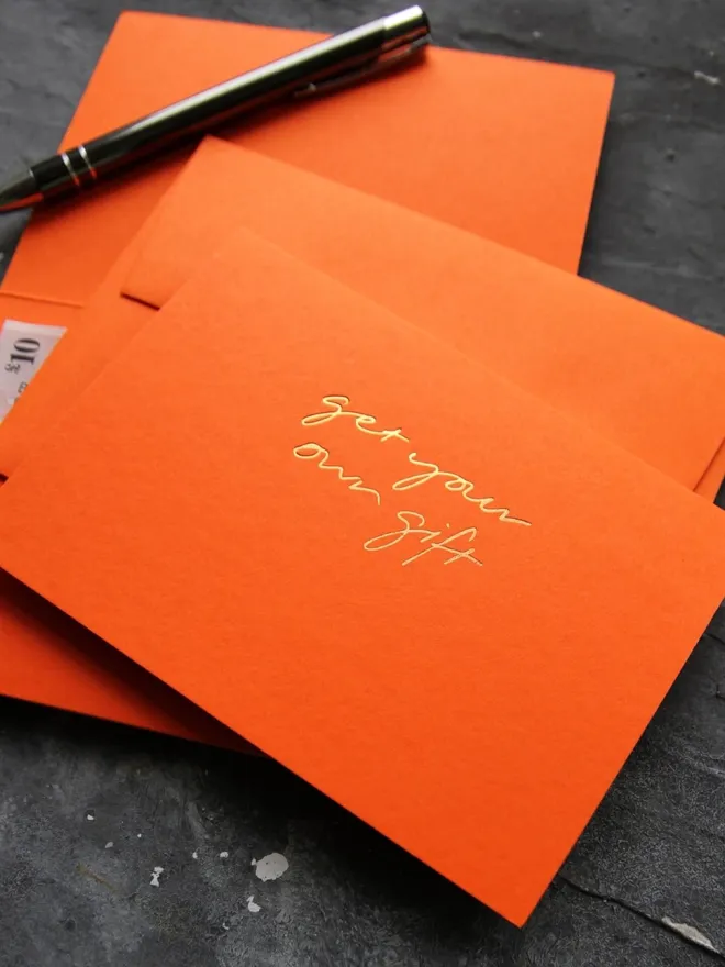 Hand foiled cash card or money wallet in a mandarin colour handfoiled in shiny golf foil text which says ‘get your own gift’.