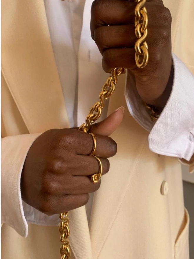a model wearing gold rings holding a heavy golden chain necklace