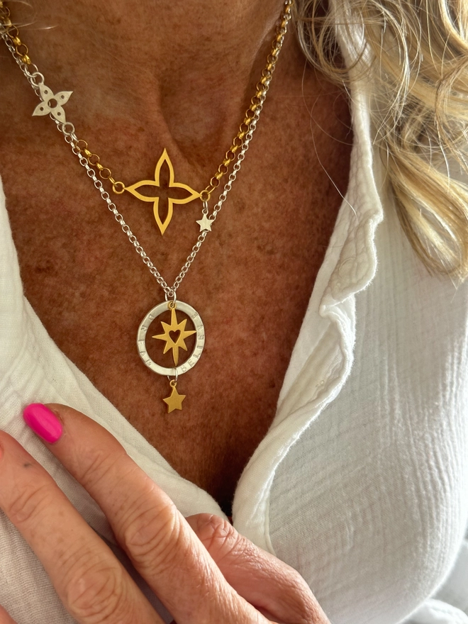 model wears a sterling silver chain with personalised silver halo charm. suspended within the halo is a gold starburst charm with cutout heart, with gold mini star suspended from the bottom of the halo