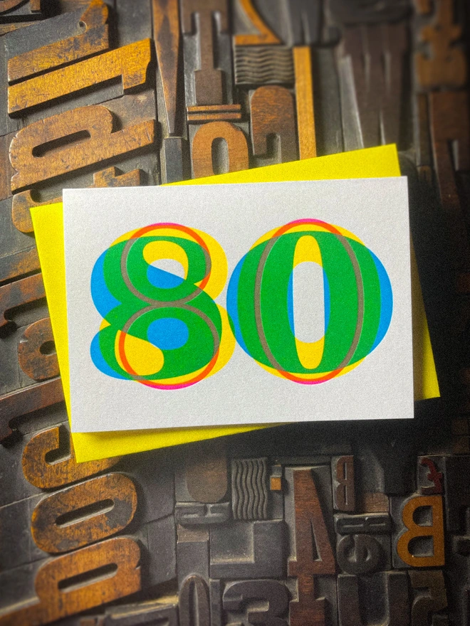 Handmade letterpress 80th birthday card featuring bold overlapping numerals printed in vibrant fluorescent cyan, magenta and yellow inks. Each card is individually hand printed using traditional letterpress techniques on luxury paper stock, creating a beautifully tactile finish with a subtle deboss and rich layered colours inspired by the CMYK printing process.