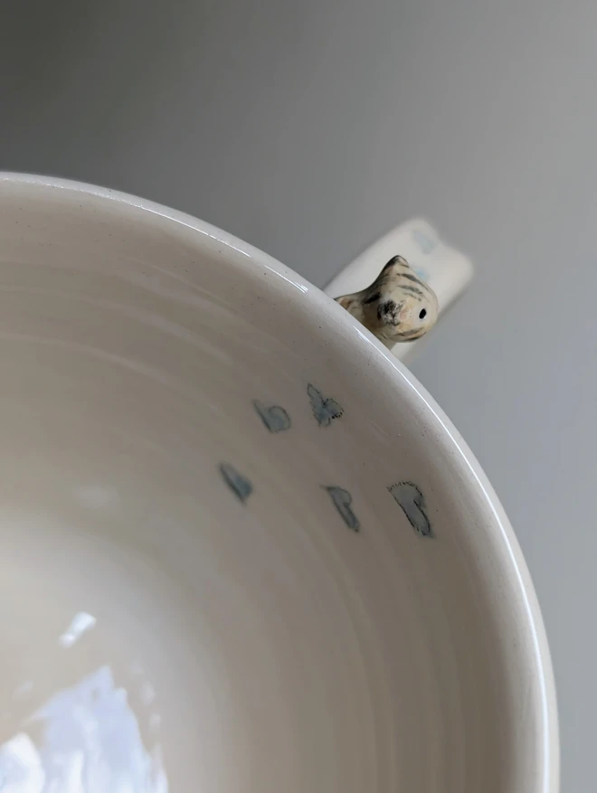 pottery cup with blue stripes and a tiny ceramic cat on the handle