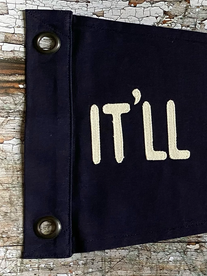 Detail of the navy 'It'll always be you' pennant flag. This shows the work 'It'll' in ivory canvas.