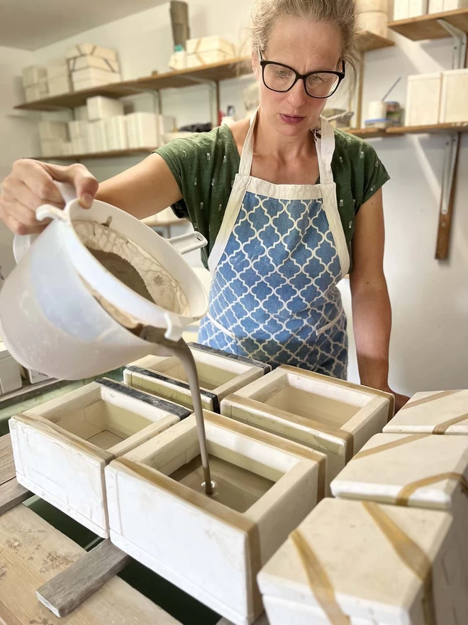 In her studio Katie is filling plaster butter dish moulds with slip (liquid clay) from a large plastic jug.