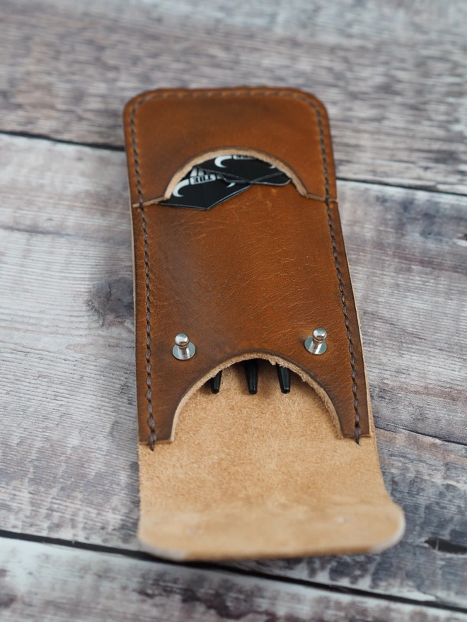 Handmade leather darts sleeve holding a set of darts and flights.