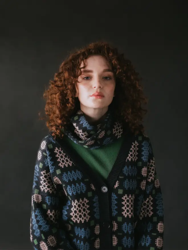 Model wearing pieces from MABLI's 'Carthen' collection, featuring the Carthen Wrap in the vibrant 'Emeralds' colour-way. The design showcases bold, colourful patterns inspired by traditional Welsh blanket tapestry.