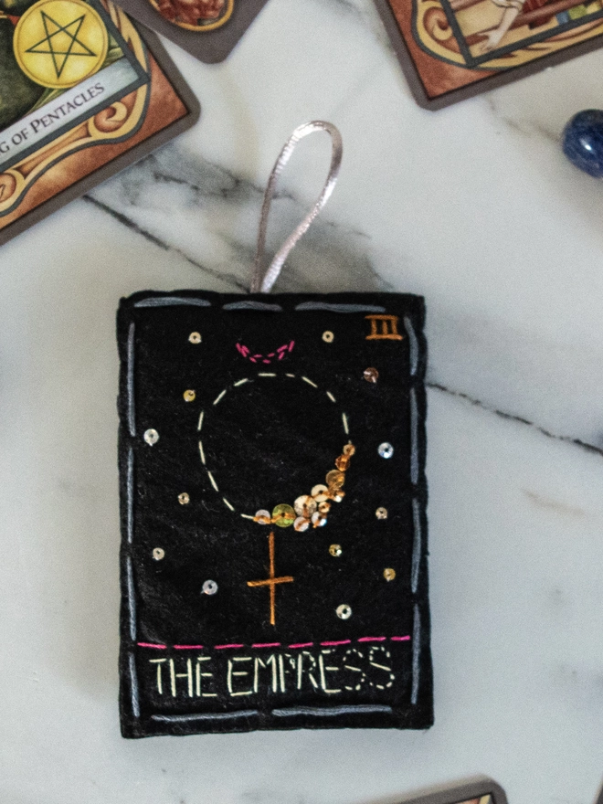 A handcrafted felt ornament with sequins and embroidery depicting "The Empress" tarot card. 