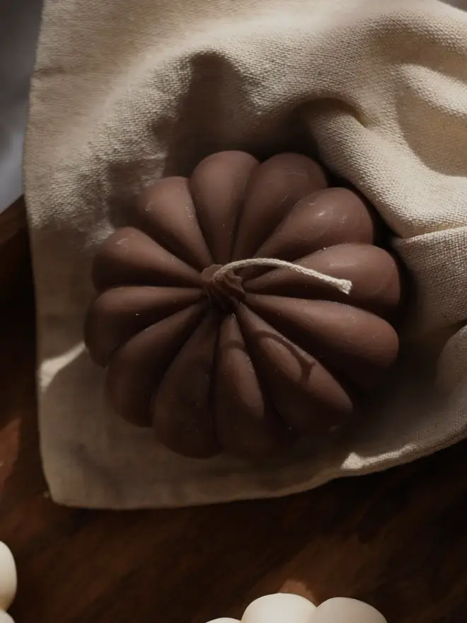 Extra Large Classic Dark Brown Wax Pumpkin Candle. Close-up of a chocolate brown pumpkin candle with deep rounded ribs and a cotton wick, nestled in a natural linen drawstring bag. The smooth sculptural shape and rich earthy tone make it a stylish autumn gift.
