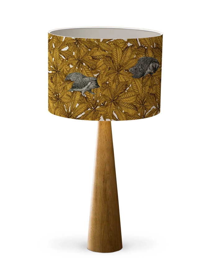 Handmade lampshade featuring cosy hedgehogs nestled among autumnal yellow leaves, creating a warm and whimsical woodland design.