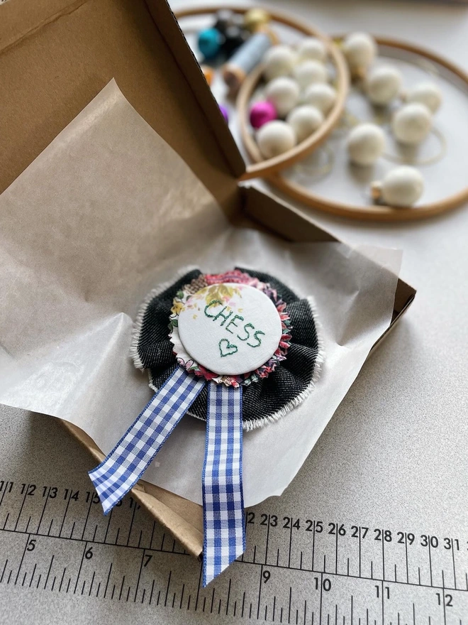 a handmade rosette, with dog's name embroidered on it, some Christmas baubles in the background