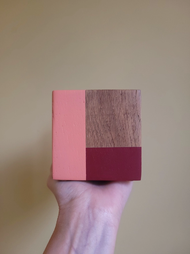Wood cube with red and pink painted L held on a soft yellow background