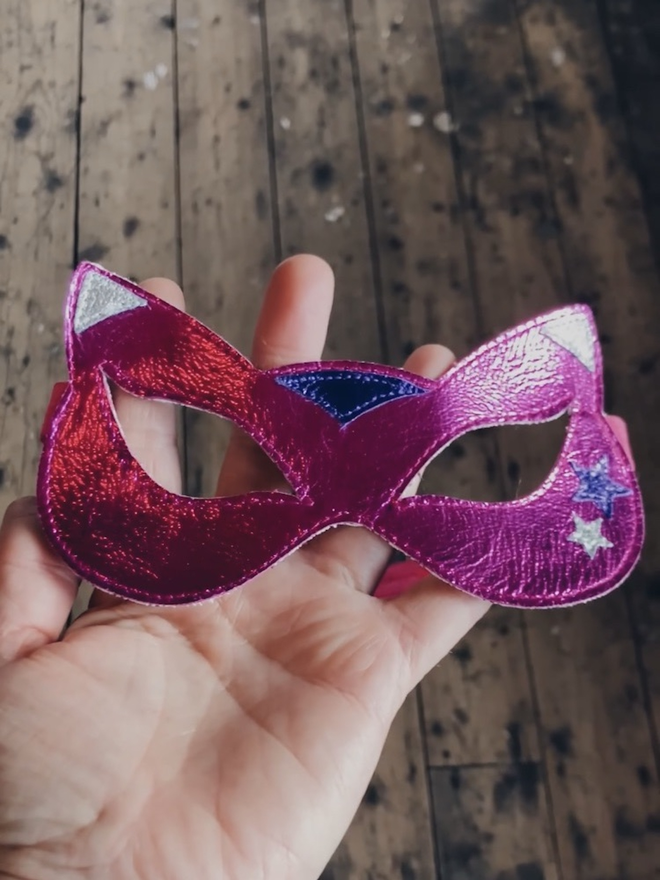 a metallic pink superhero cat mask in a hand