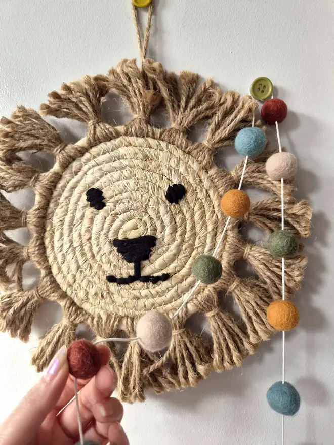 Felt ball garland hanging on a wall with a rattan lion in the background.