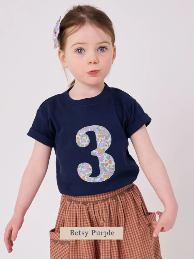 a 3 year old girl wearing a navy birthday t-shirt with a number 3 cut from liberty floral print on the front