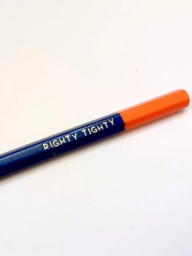 Close up of a pencil with an orange top with 'righty tighty' written in gold.