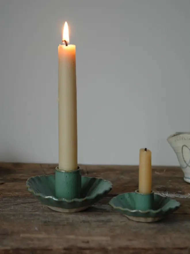 Handmade Green Ceramic Candlestick Holder, a pair of green candlestick holders sitting on a wooden surface. They are accompanied by some lit candles. 