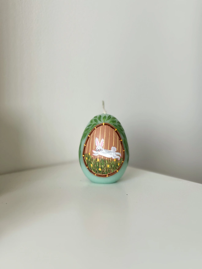 Hand Painted Easter Egg Candle Bunny, an Easter egg candle sitting on a plain surface. It's Easter and floral design wraps around it. 