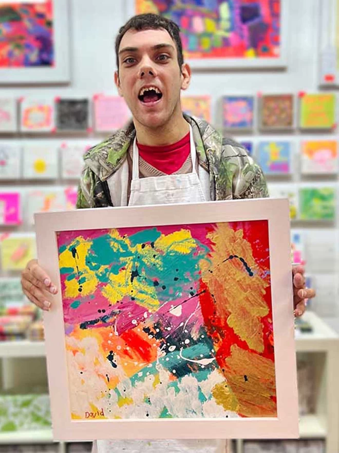 Happy artist holding framed original abstract artwork in bright colours to go on charity chocolate bars