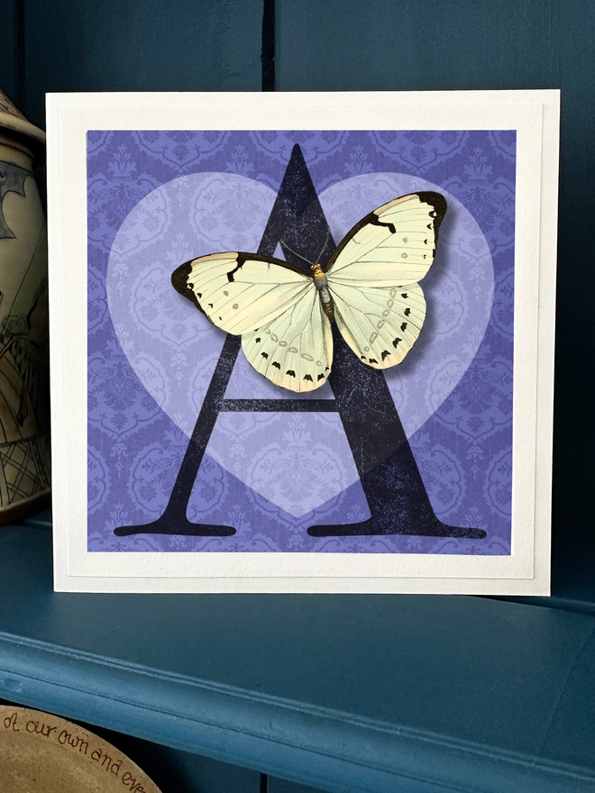 Valentines Day card showing the letter A whuch can be personalised for the initial of recipient. The letter sits against a blue background with a light blue heart. Sitting on the letter A is a white paper cut butterfly. The wings can be folded outwards when on display.