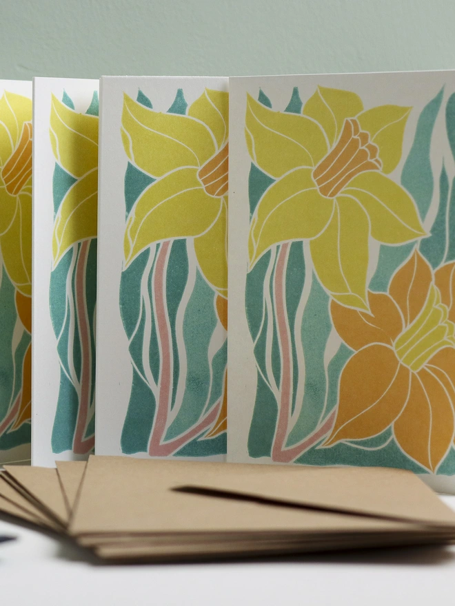 Set of 8 hand-carved botanical notecards featuring the Welsh Daffodil. A6 linocut print greeting cards in spring yellow and teal, displayed with kraft envelopes. Cottagecore stationery on recycled cardstock.