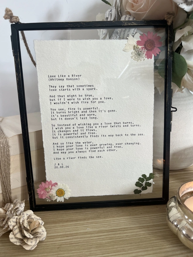 Framed typewriter print hand typed with an antique typewriter onto cotton rag handmade deckled paper. It is displayed in a black hanging rustic frame with gold brush detailing and decorated with real pressed dried flowers.