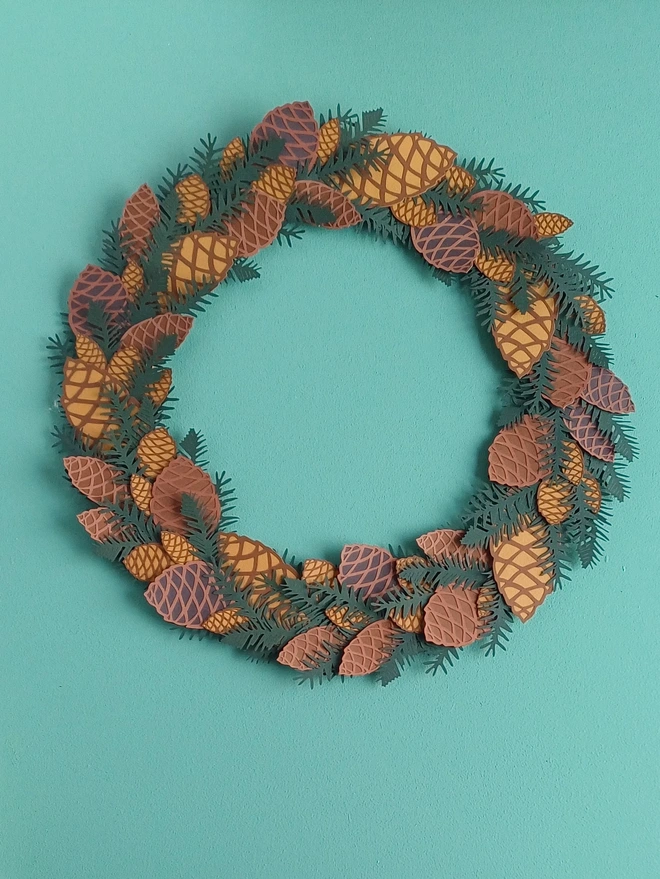 Papercut Pinecone Wreath displayed on blue/green wall