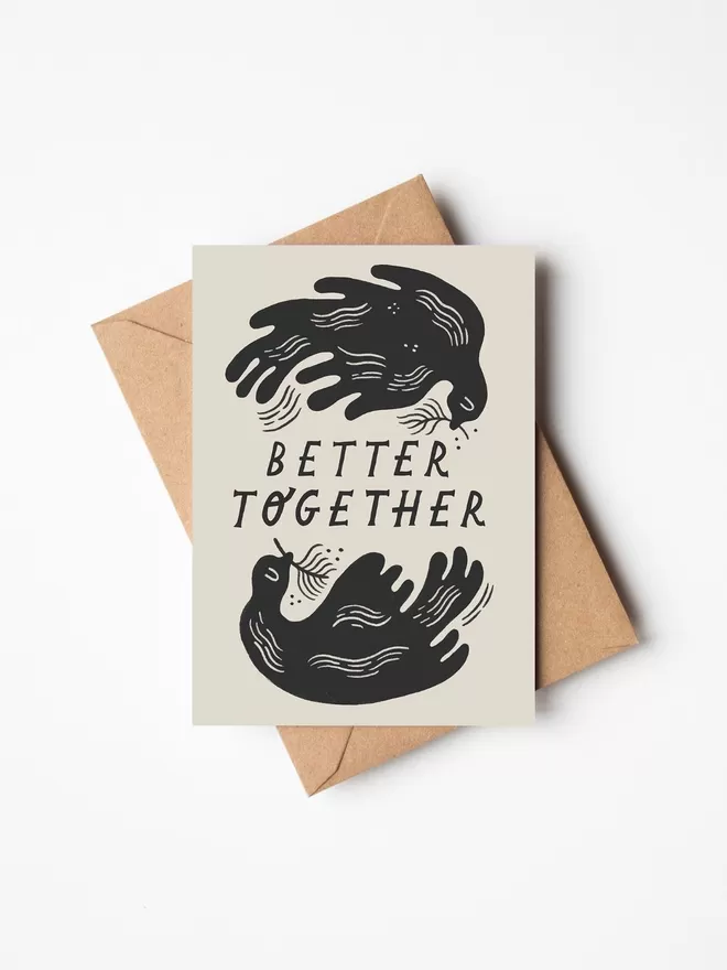 Black and white greeting card with illustration and the words better together written on it with a brown envelope underneath it. 